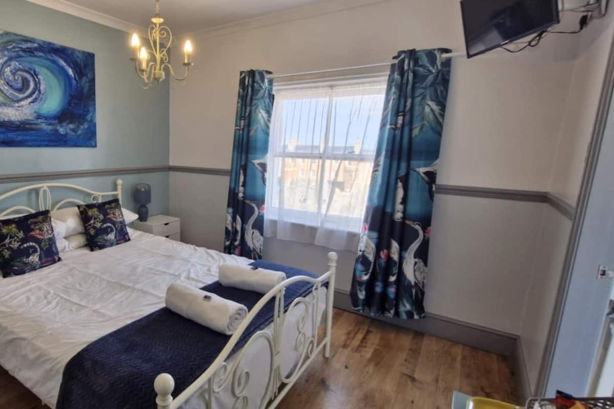 A bedroom with a bed, nightstands, a chandelier, a painting, and curtains.