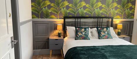 A bedroom with a bed, nightstands, and a wall with a leafy pattern.