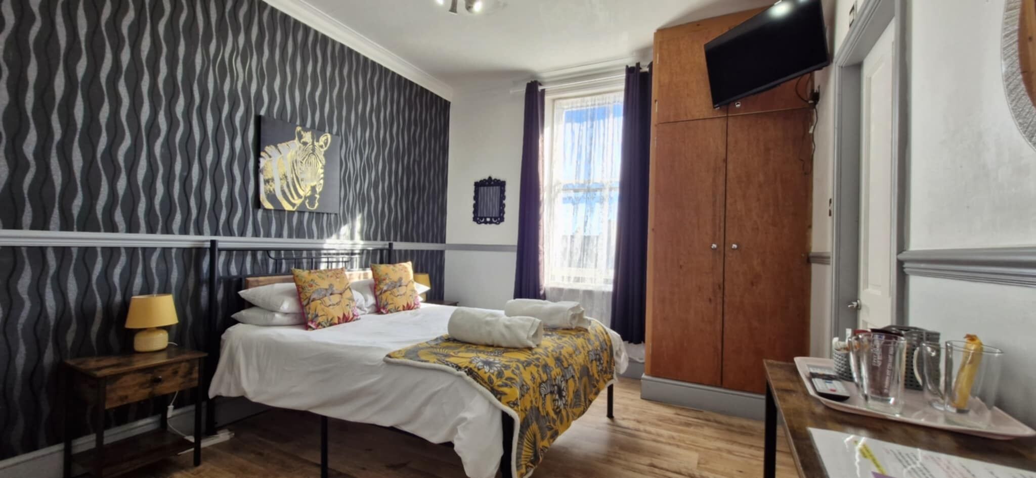A hotel room with a bed, a bedside table with a lamp, a wardrobe, and a window with curtains.