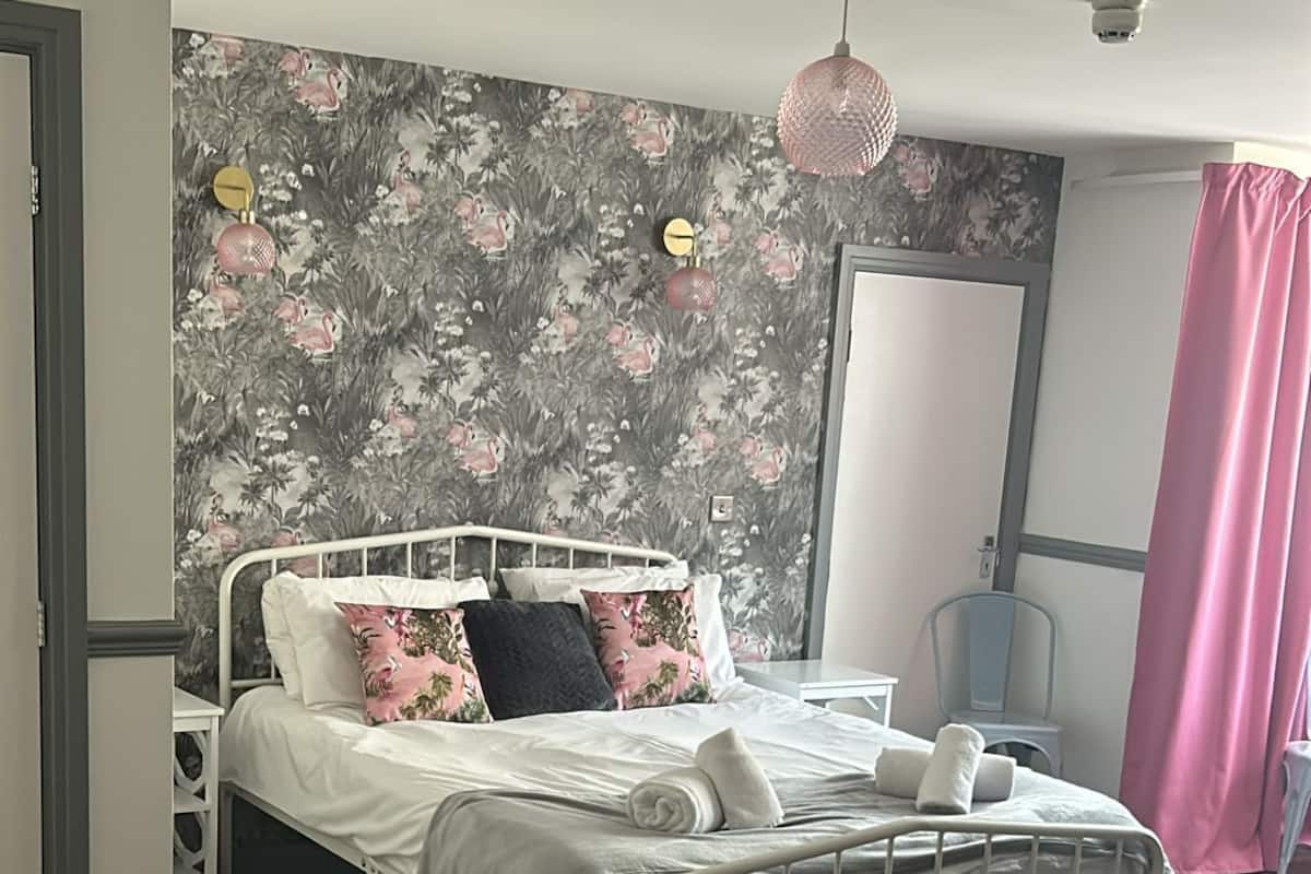 A neatly made bed with white linens and pink floral pillows, a white metal bed frame, and a wooden floor.
