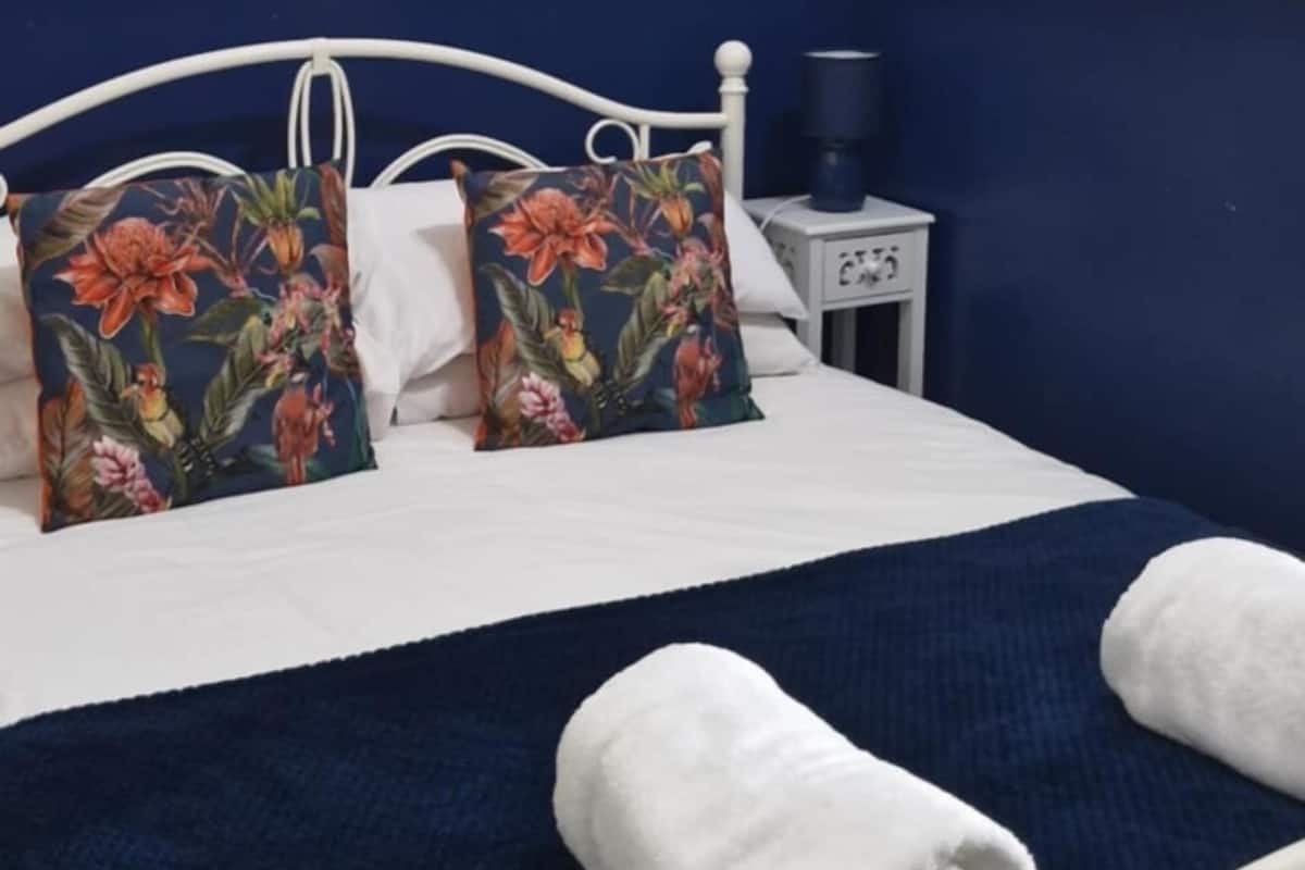 A bed with floral pillows, a white blanket, and a rolled towel.