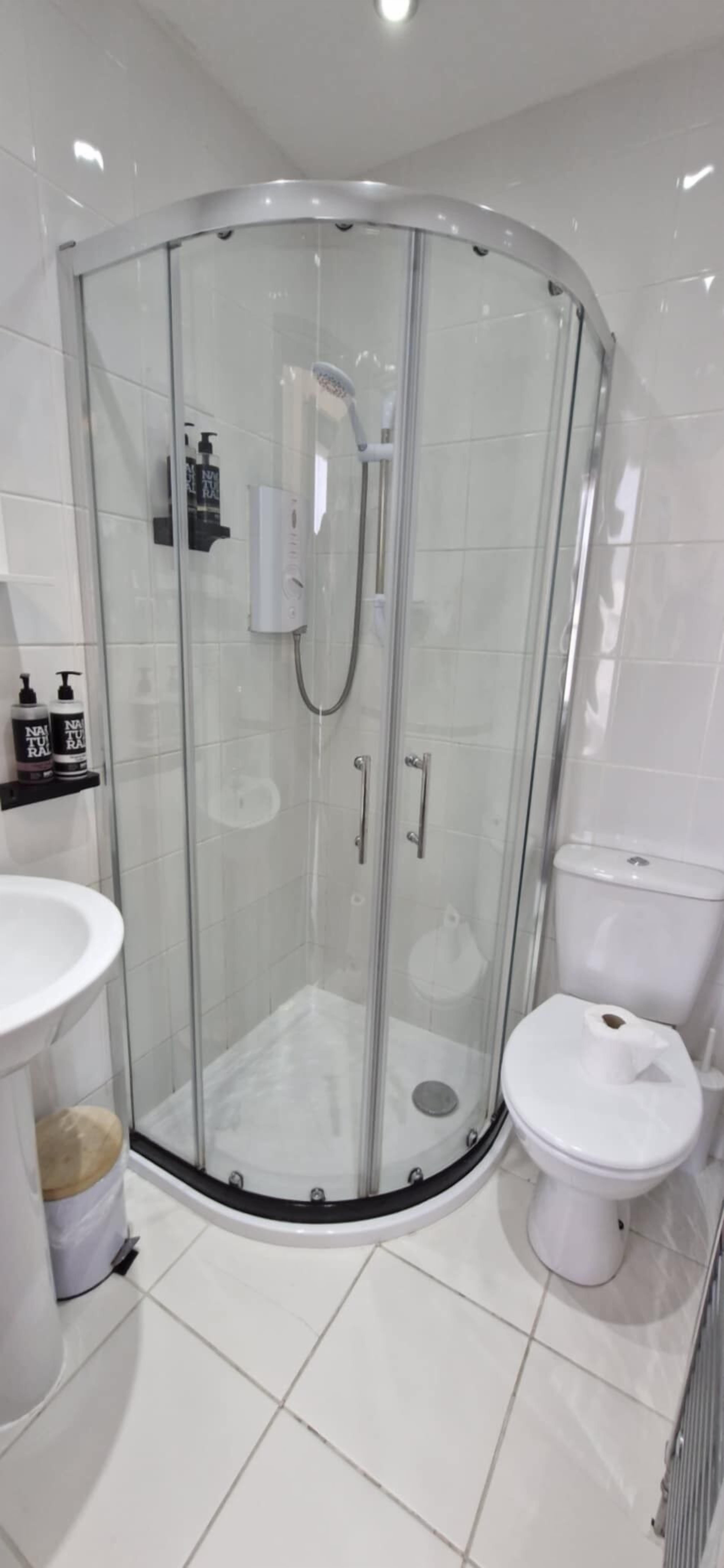 Un baño moderno con ducha de vidrio, inodoro blanco y lavamanos con encimera color crema.