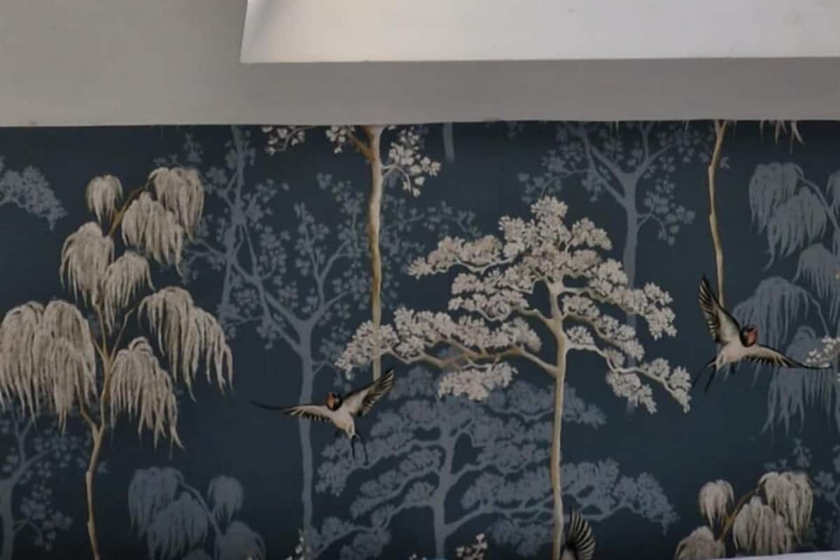 A room with a skylight, a floral wallpaper, and a cushion with a bird design.