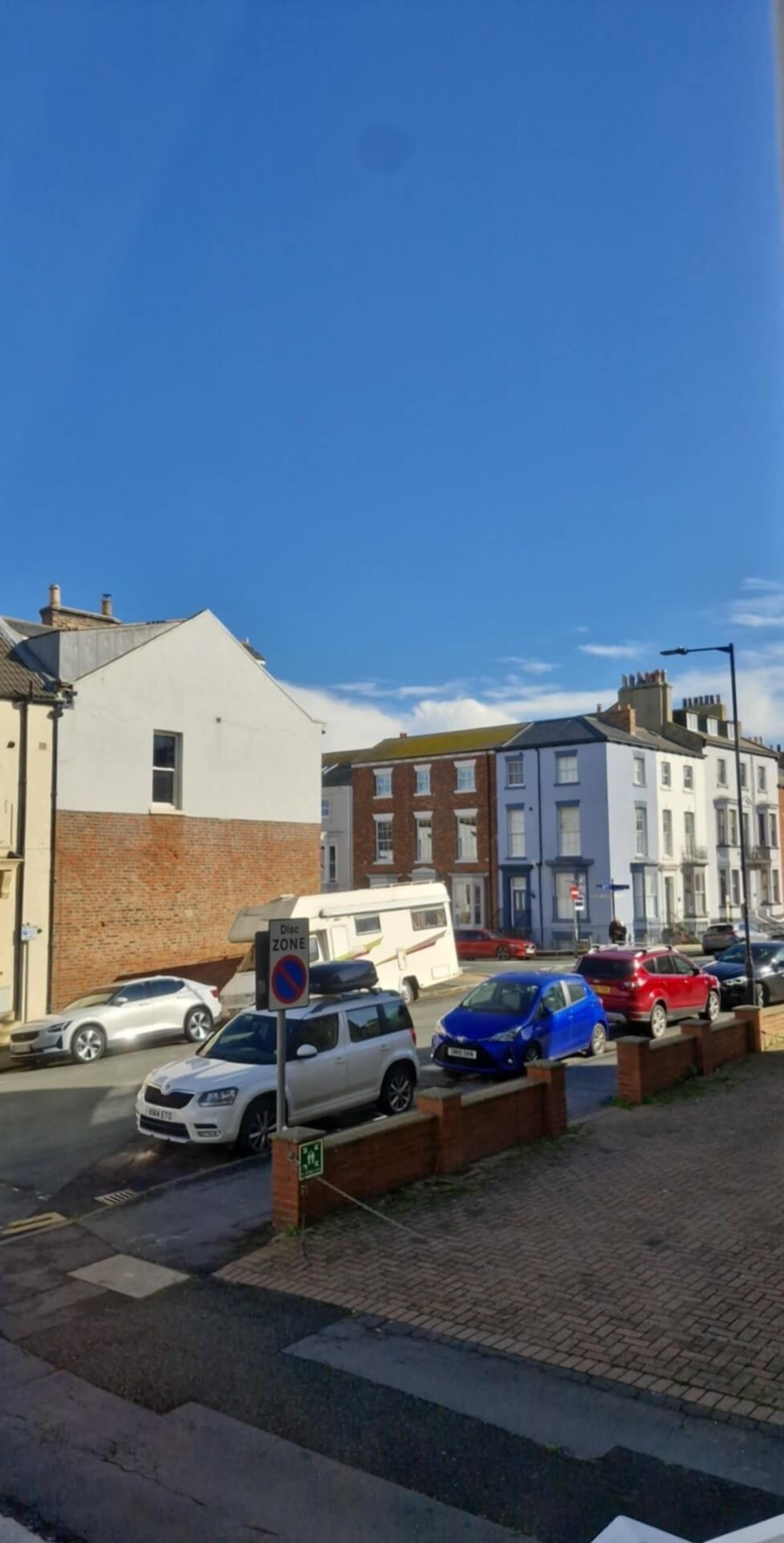 A street with parked cars, a white building, and a blue car.