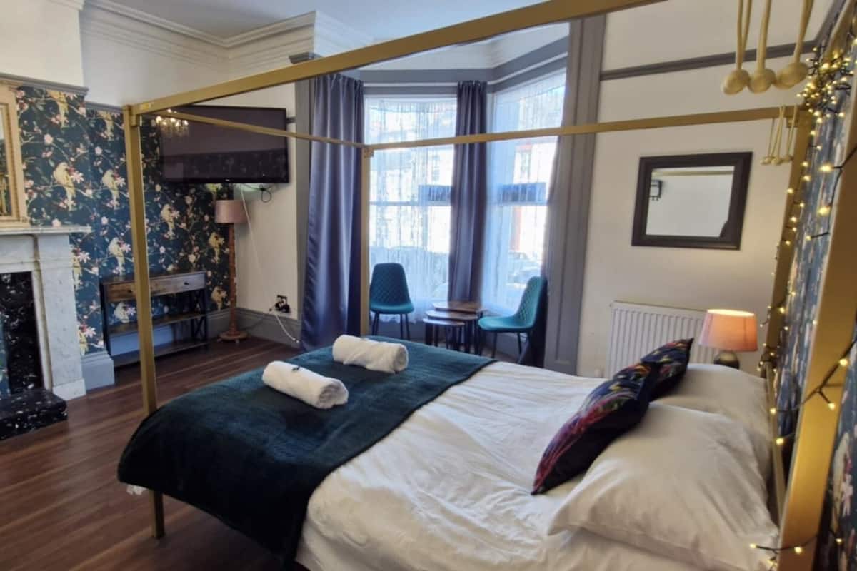 A bedroom with a four-poster bed, a fireplace, and a view of the city.