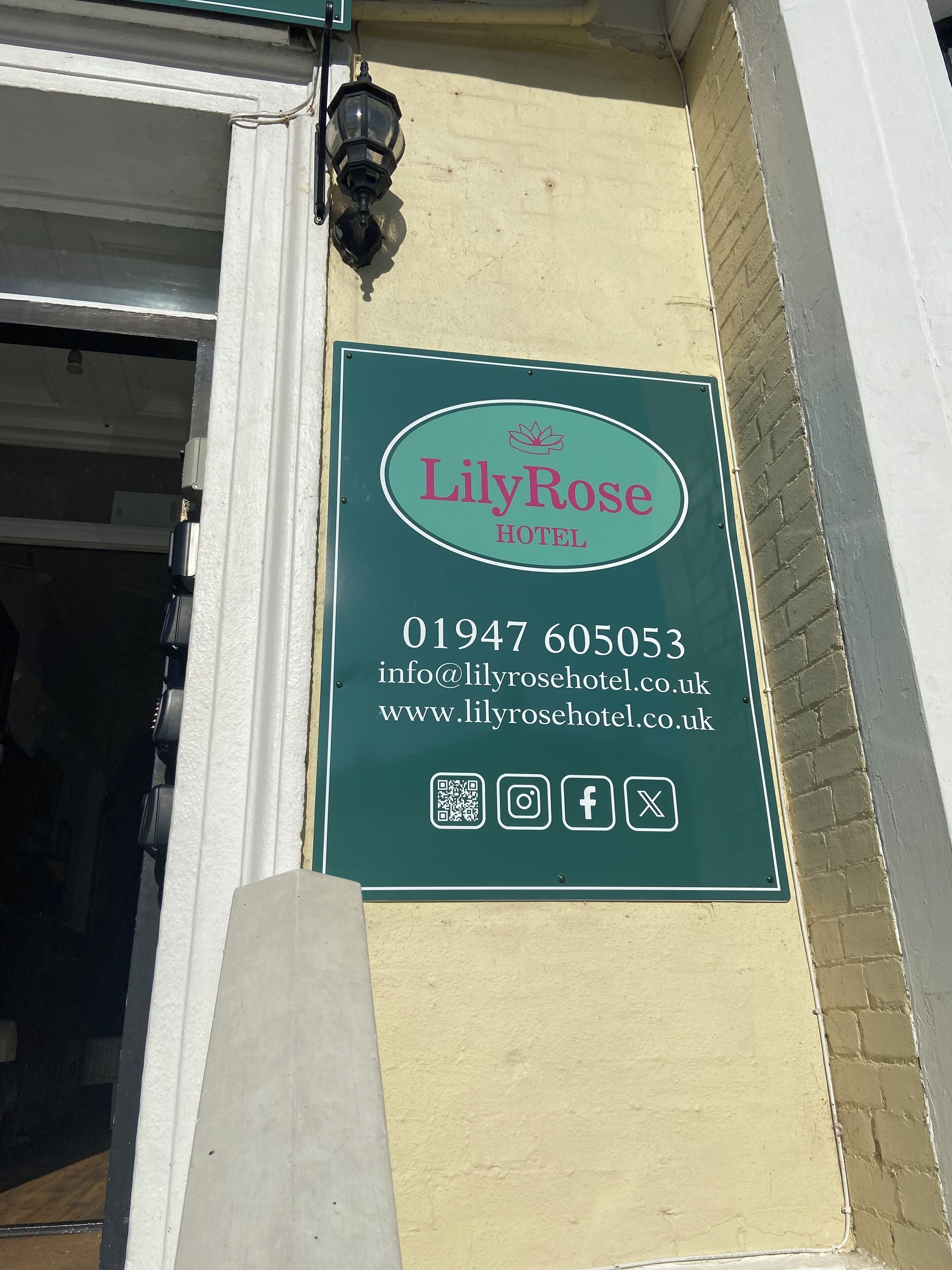 Schild des LilyRose Hotels mit Kontaktinformationen und Social-Media-Symbolen.