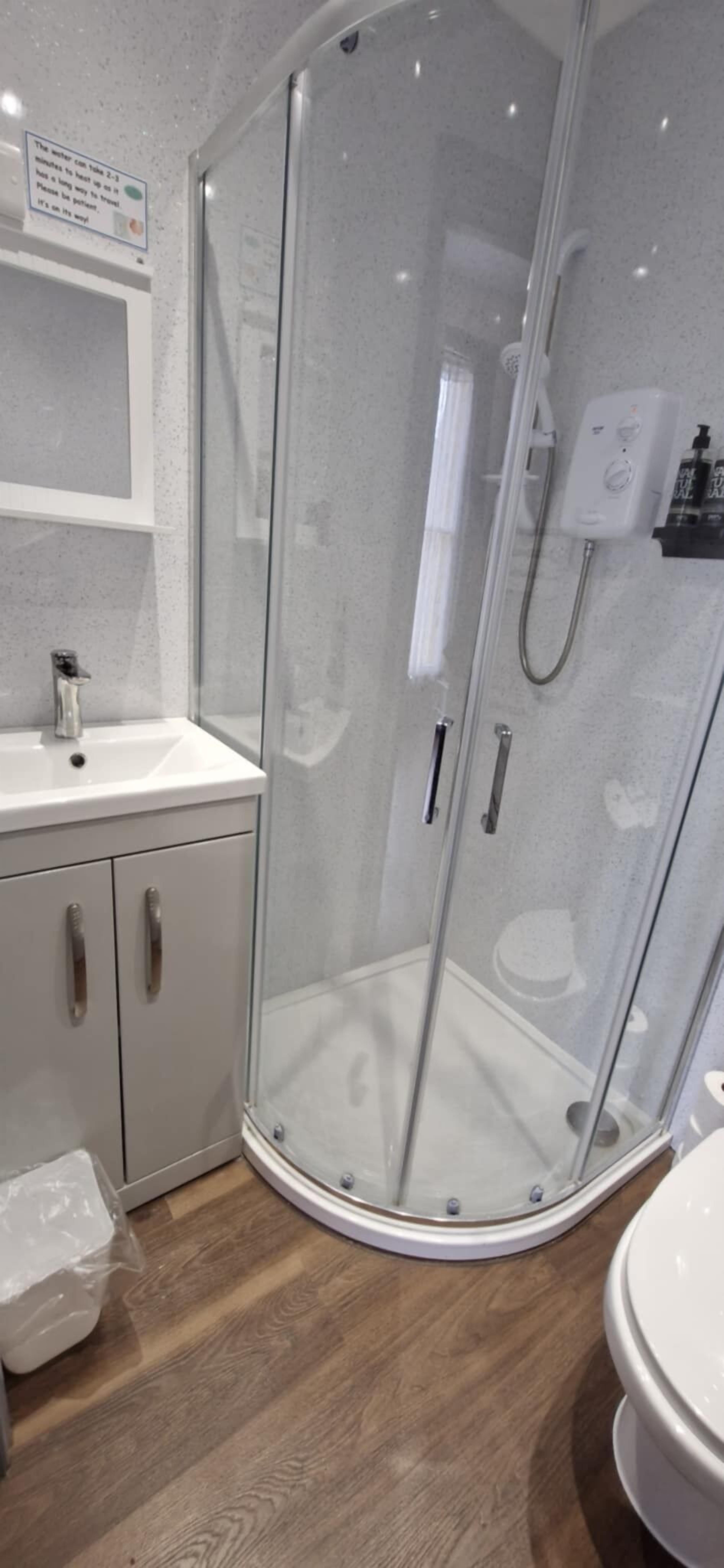 Ein modernes Badezimmer mit einer Glasdusche, einem weißen Waschbecken und Holzboden.