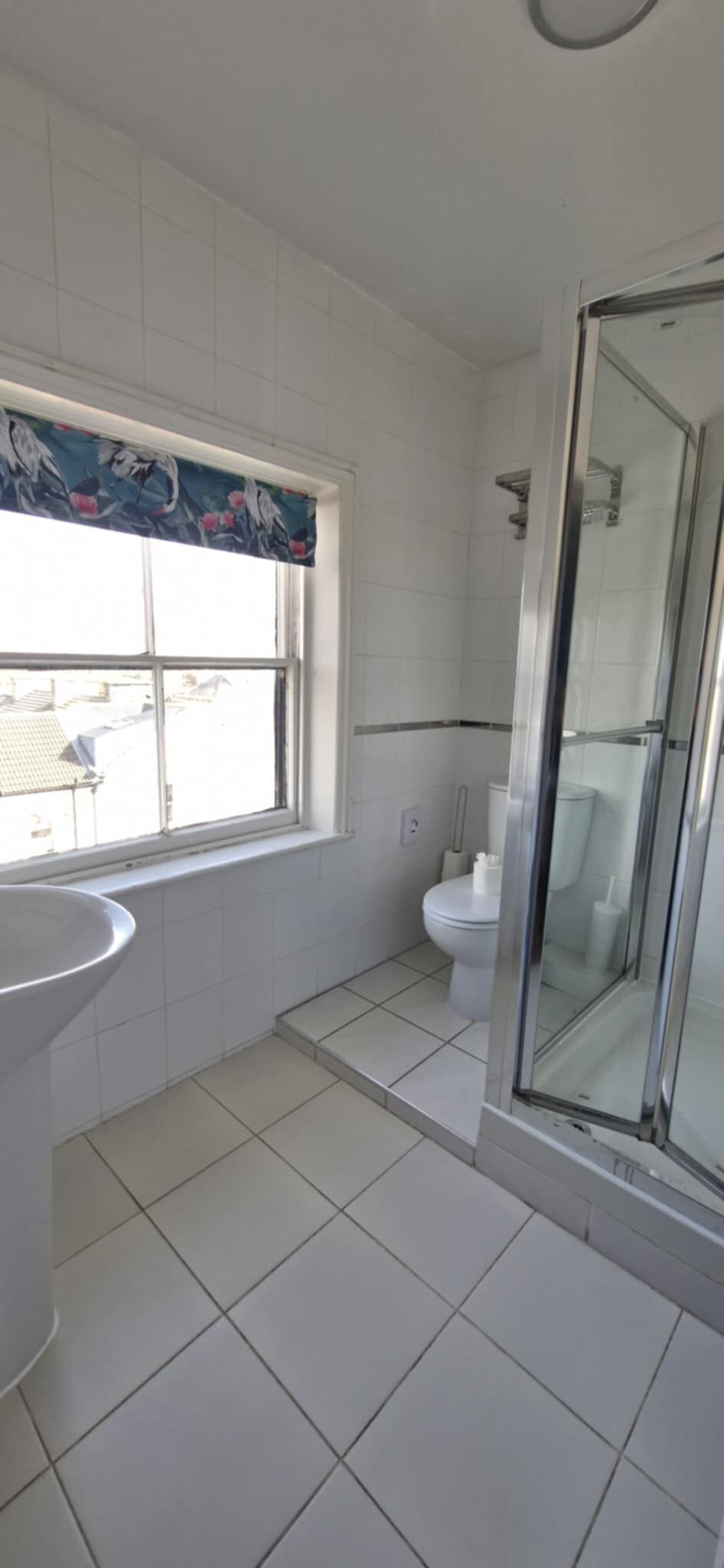 A bathroom with a window, a toilet, a shower, and a sink.