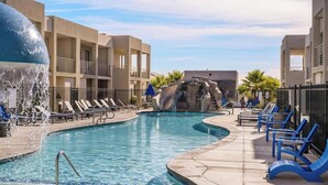 A swimming pool with a water feature, lounge chairs, and a building with balconies. - Tranquility at The Lofts Near National Parks (St. George)