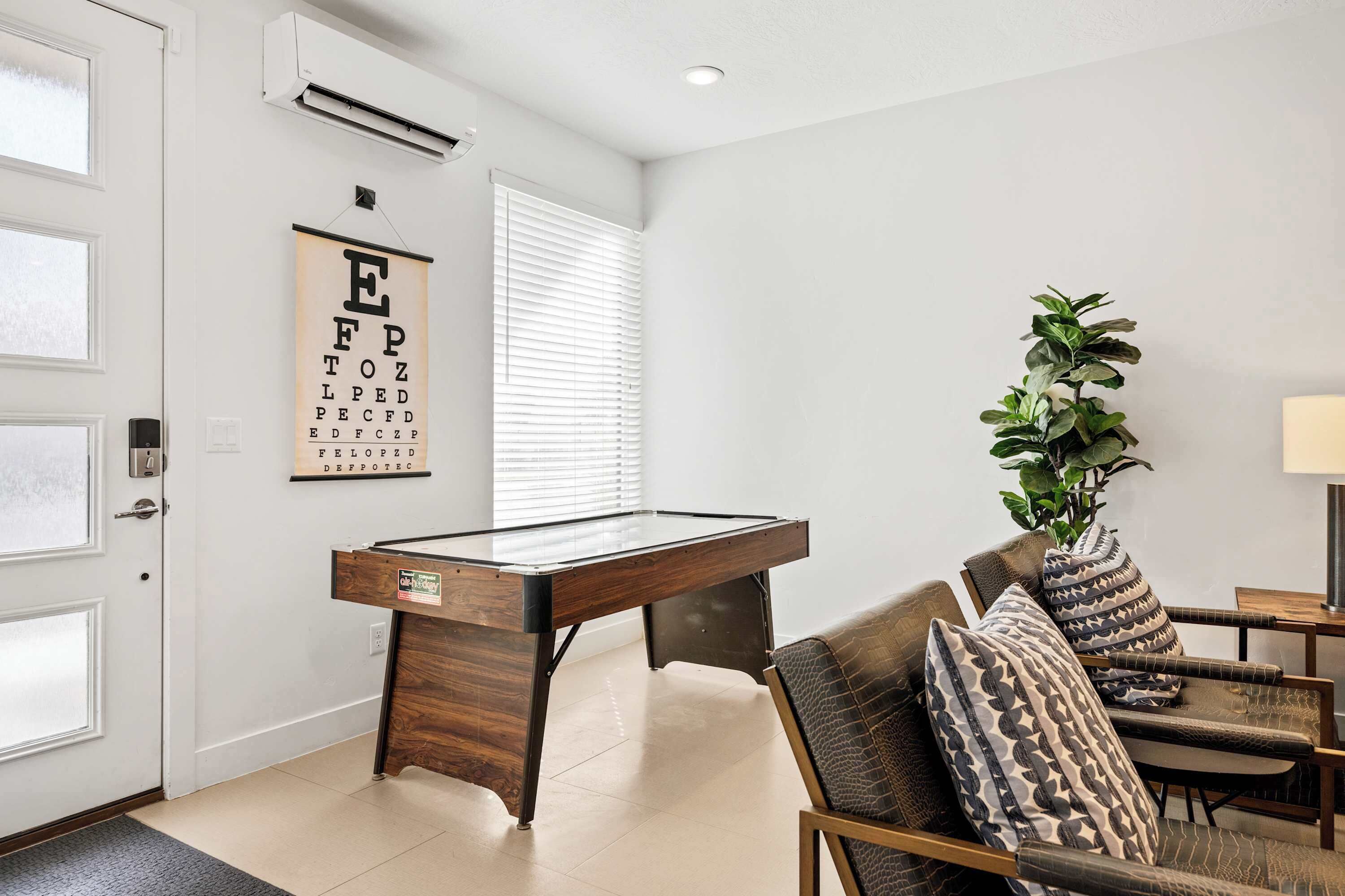 A modern living room with a pool table, a comfortable sofa, a potted plant, and a wall-mounted air conditioning unit.