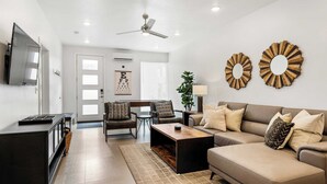 A modern living room with a sofa, coffee table, and TV. There is a ceiling fan, a door with frosted glass panels, and a wall-mounted mirror. - Tranquility at The Lofts Near National Parks (St. George)