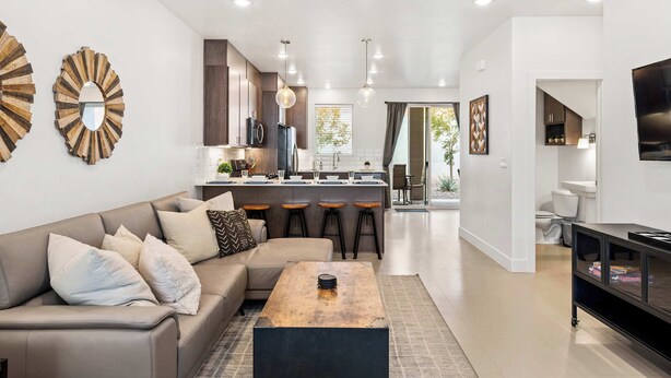 A modern living room with a sofa, coffee table, and kitchen in the background. - Tranquility at The Lofts Near National Parks (St. George)