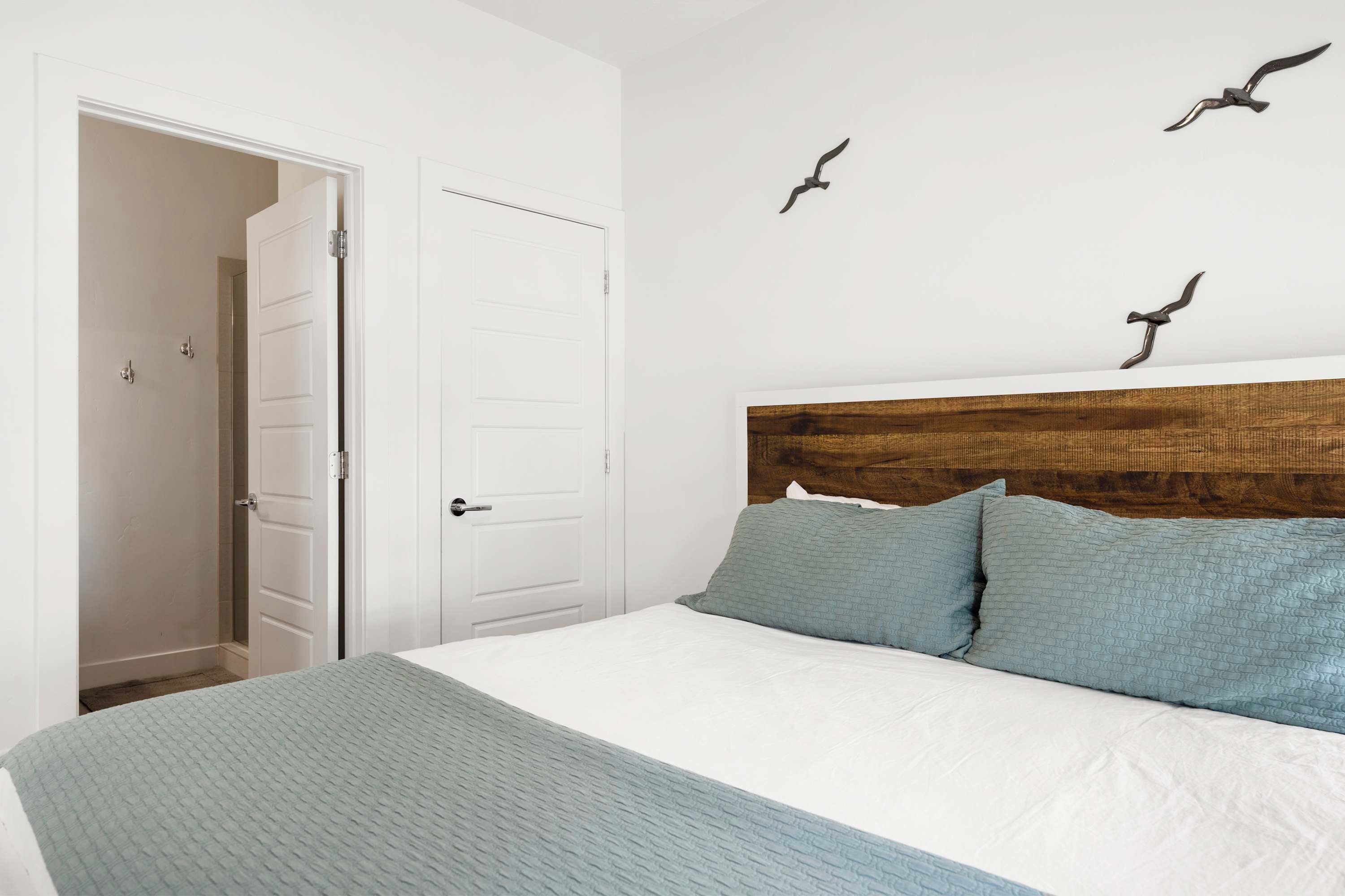 A bedroom with a white bed, two pillows, a wooden headboard, and three bird wall art pieces.