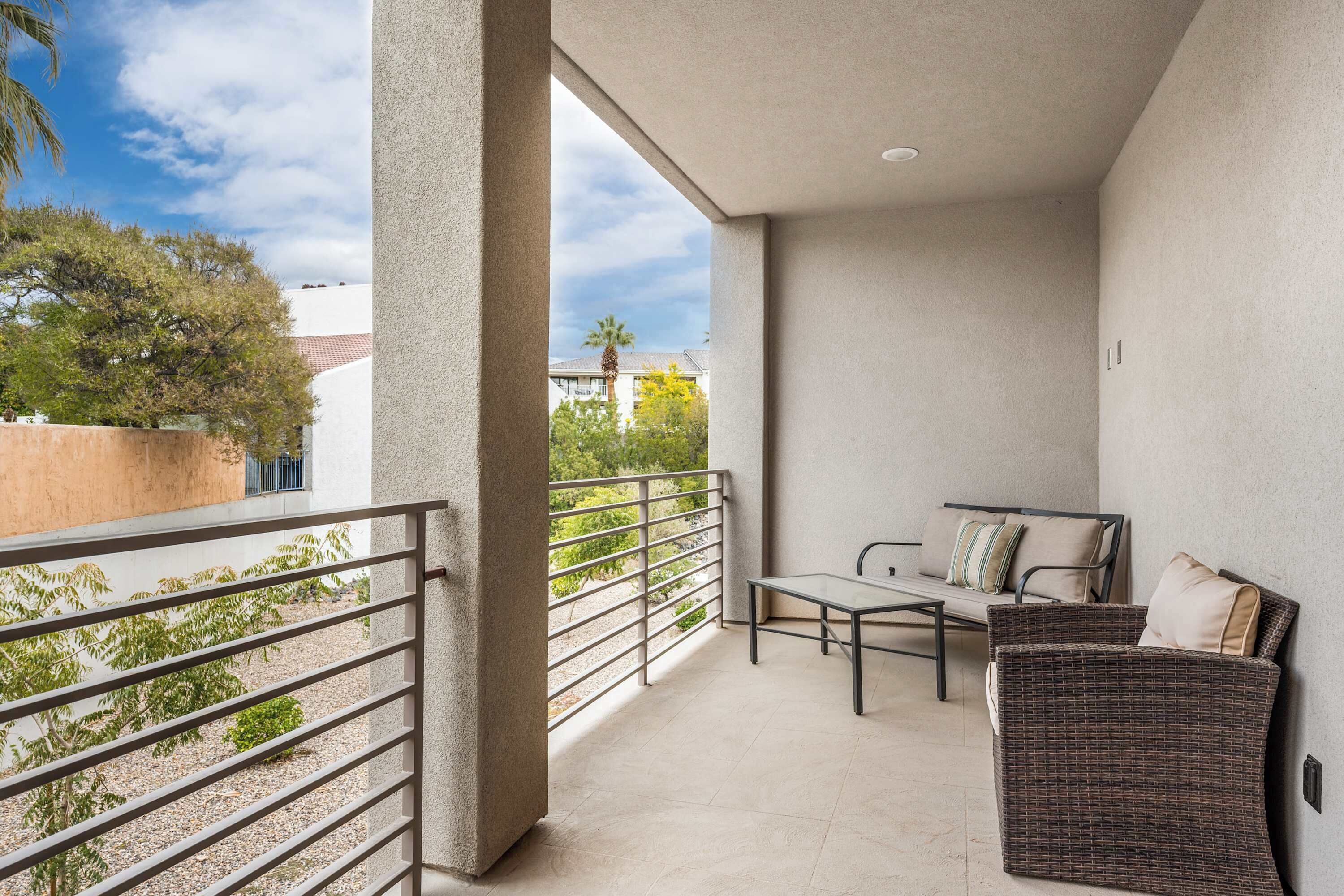 A balcony with a wicker sofa, a small table, and a metal railing.