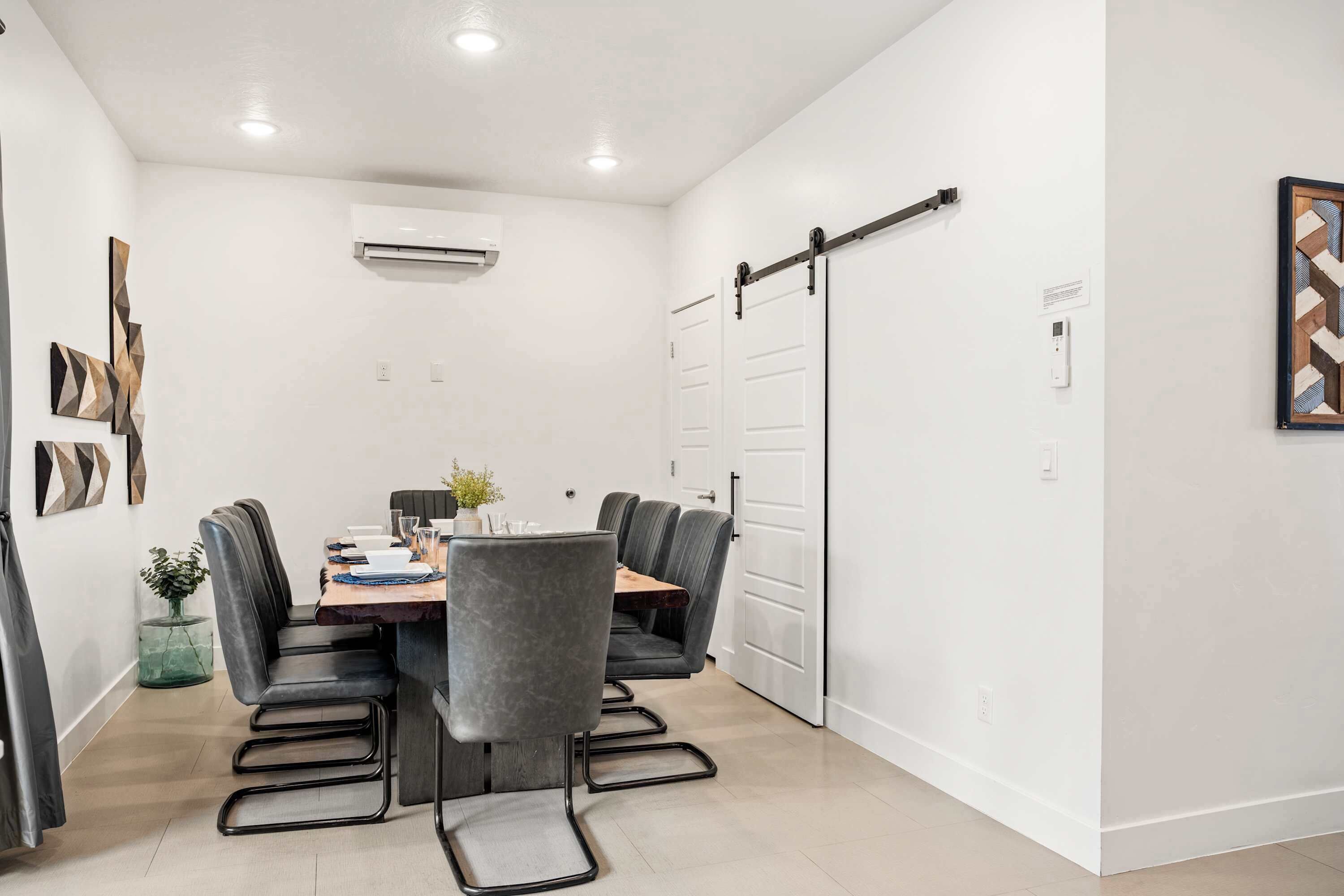 A modern dining area with a rectangular table, six grey upholstered chairs, and a wooden bench.
