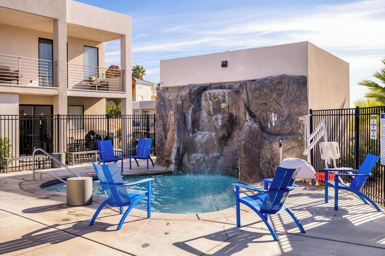 A pool area with blue chairs, a rock wall, and a building with balconies.