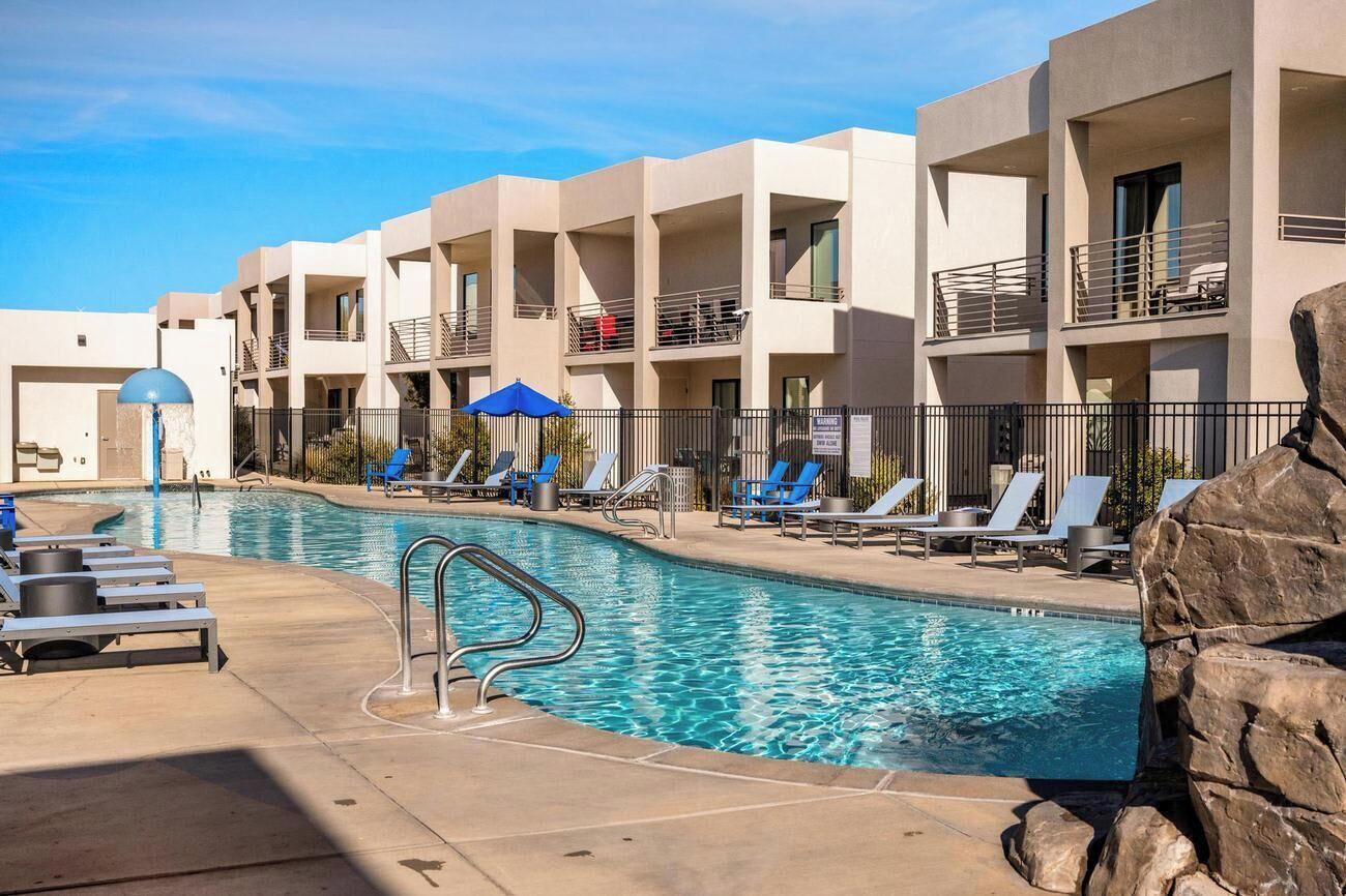 A swimming pool area with lounge chairs and umbrellas, surrounded by multi-story buildings with balconies.