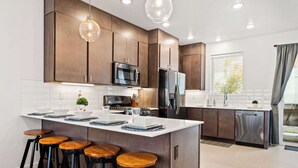 A modern kitchen with dark wooden cabinets, stainless steel appliances, and a central island with stools. - Tranquility at The Lofts Near National Parks (St. George)