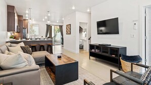 A modern living room with a sofa, coffee table, and TV. There is a kitchen area with a bar and a dining table. - Tranquility at The Lofts Near National Parks (St. George)