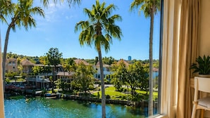 Una habitación con un gran ventanal que da a una masa de agua, palmeras y una zona residencial.