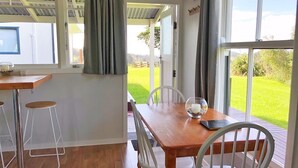 A dining area with a wooden table, white chairs, and a view of a green landscape through large windows.