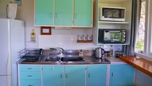 A kitchen with teal cabinets, a stainless steel sink, a microwave, and a toaster.