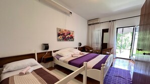 Una camera da letto con due letti, un quadro, un condizionatore d'aria, una finestra con tende e vista sul verde.