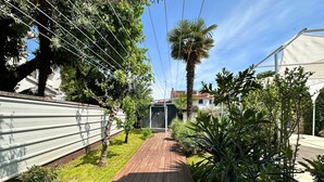 Un vialetto in legno conduce a una casa con un cortile recintato, una palma e un capanno.