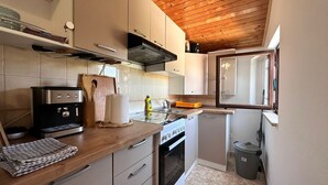 A compact kitchen with a wooden ceiling, a built-in oven, a coffee maker, and a small trash bin. - Apartments Cocolo - Superior One Bedroom Apartment with Terrace (Porec)