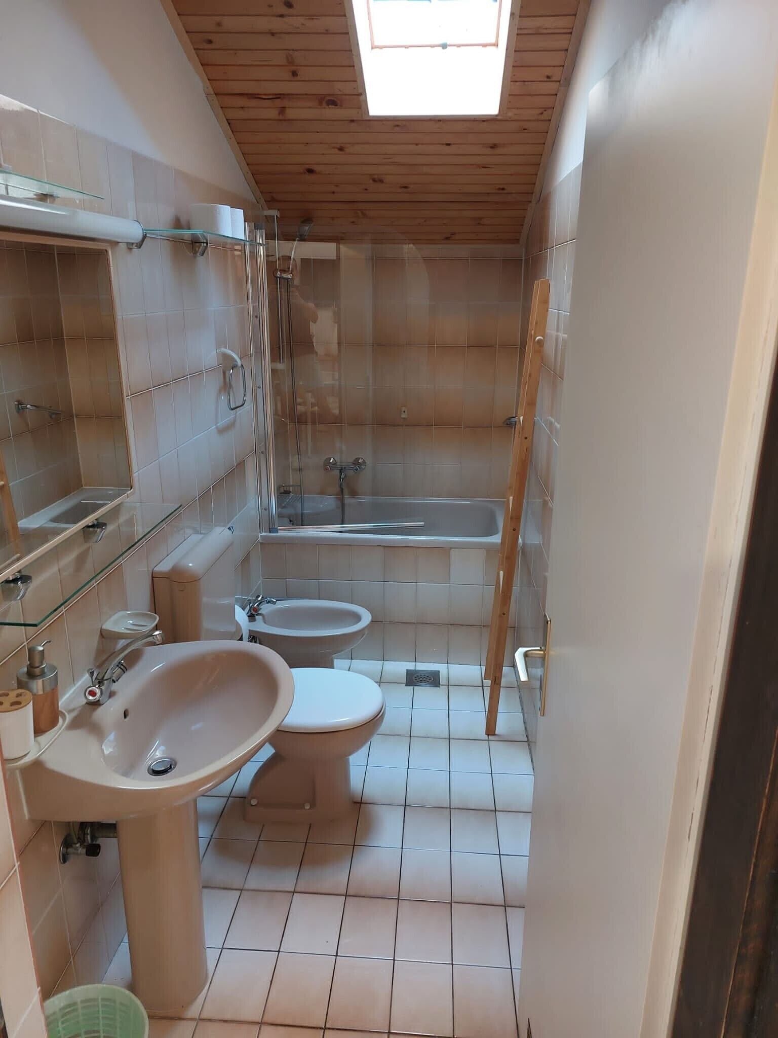 A compact bathroom with a skylight, a bathtub, a sink, and a toilet.