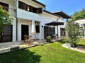 A two-story house with a balcony, a patio with outdoor furniture, and a small garden area.