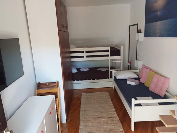 A compact bedroom with bunk beds, a desk, a chair, a bedside table, and a large window.