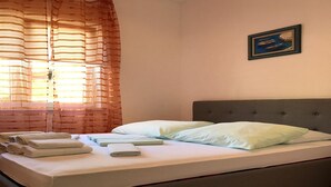 Un lit bien fait, avec des oreillers et des serviettes pliées, une tête de lit rembourrée de couleur grise et un tableau encadré accroché au mur.