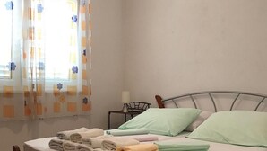 A neatly made bed with folded towels, a bedside table with a lamp, and a window with patterned curtains. - Apartments Semafor - One Bedroom Apartment with Terrace and Sea View A3 (Seget Vranjica)