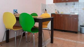 A compact kitchen with wooden cabinets, a tiled backsplash, and a dining area with a table and colorful chairs. - Apartments Semafor - One Bedroom Apartment with Terrace and Sea View A4 (Seget Vranjica)