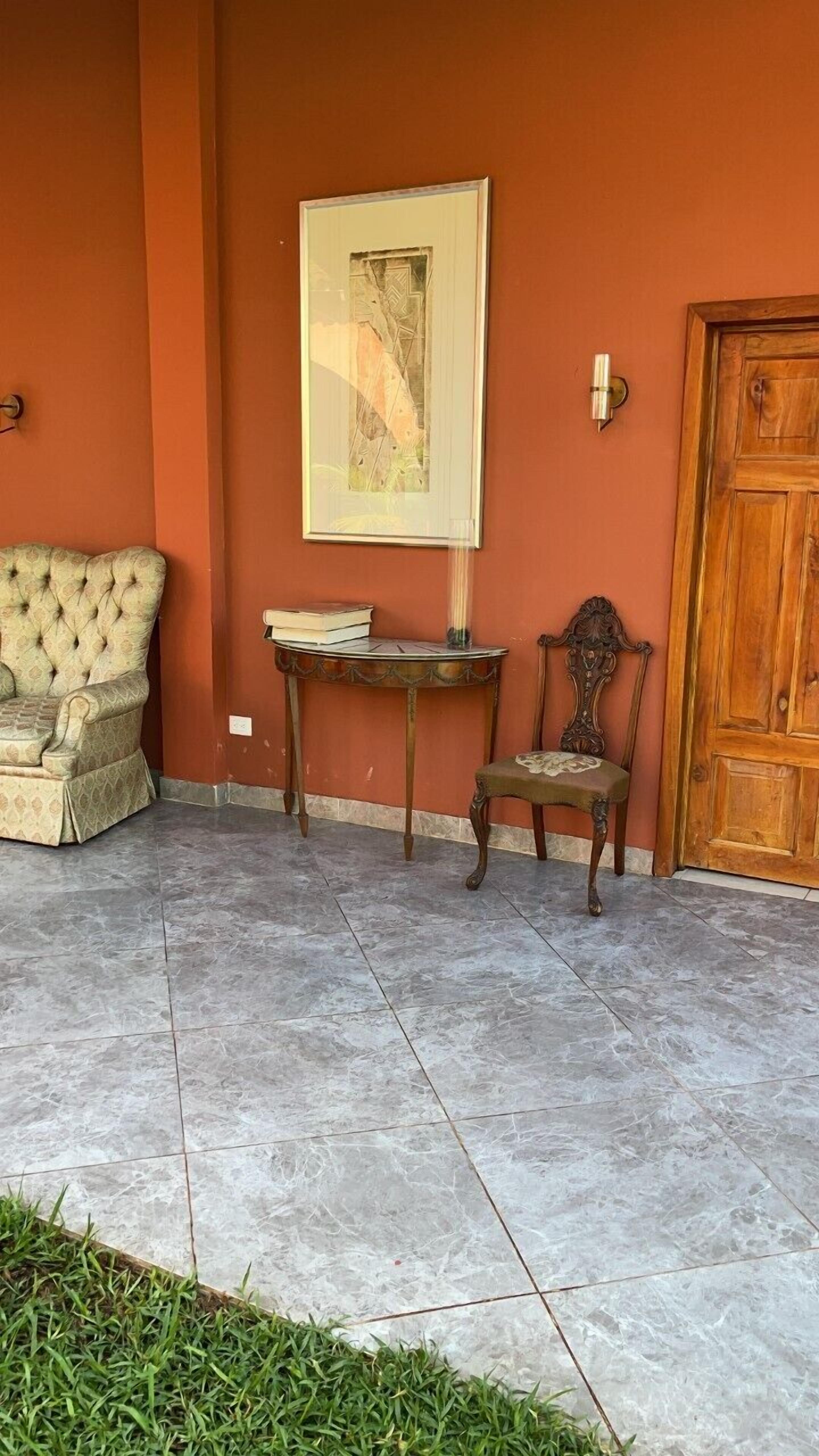 Una stanza con una poltrona trapuntata, un tavolo di legno con libri, una sedia e una porta.