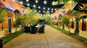 An outdoor dining area with tables and chairs, surrounded by palm trees and string lights. - Sambo Mambo Beach Hotel (El Cuco)