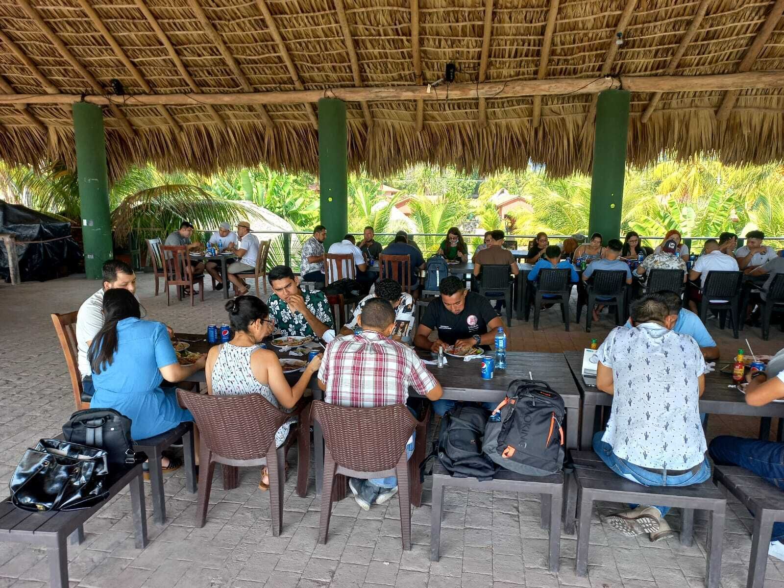 Un área de comedor al aire libre con techo de paja, mesas y sillas.