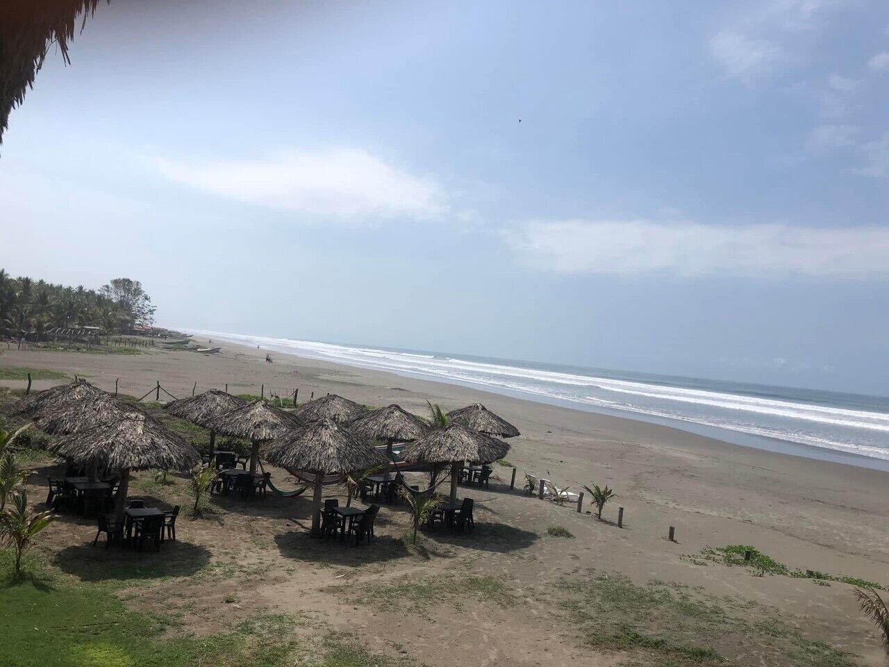 A beachside area with thatched umbrellas and tables, overlooking the ocean.