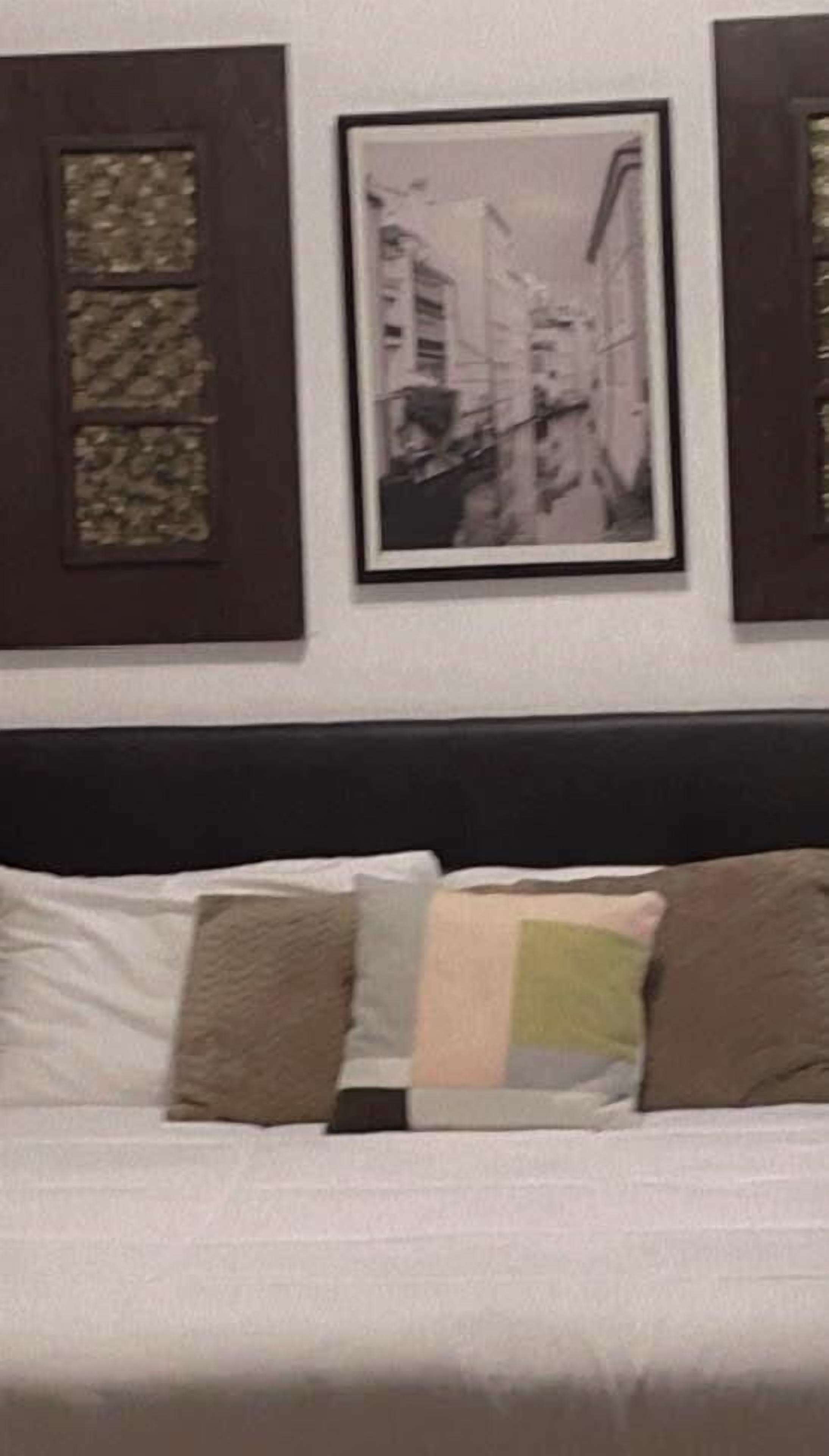 Ein Bett mit weißer Bettwäsche und mehreren Kissen, ein dunkles Kopfteil und ein gerahmtes Foto an der Wand.