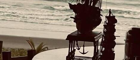 A table with a stack of chairs and a hanging light fixture, overlooking the ocean.