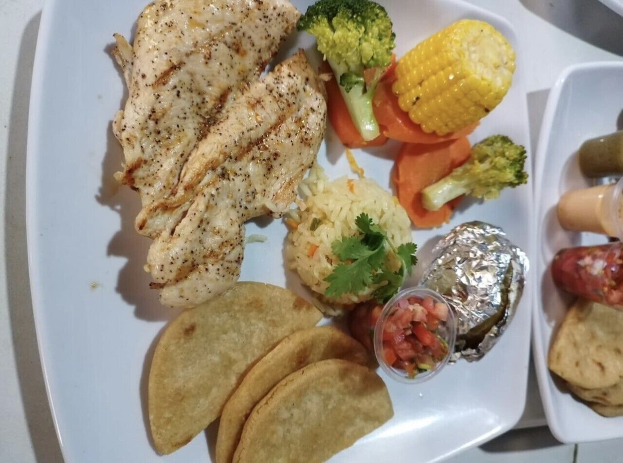 En tallrik med grillad kyckling, majs, broccoli, morötter, tortillas och en liten skål med salsa.