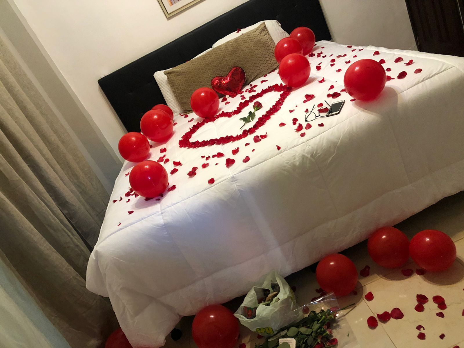 Uma cama decorada com balões vermelhos, pétalas de rosa e um enfeite em formato de coração.