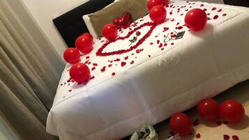 Uma cama decorada com balões vermelhos, pétalas de rosa e um enfeite em formato de coração.