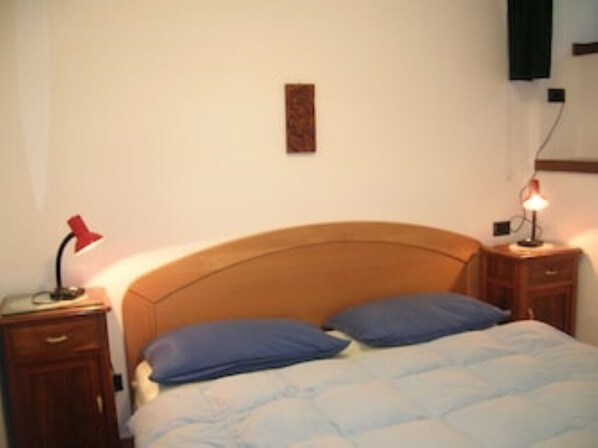 A bedroom with a wooden headboard, a bed with blue bedding, two bedside tables with lamps, and a wall-mounted TV. - Demadonna "PUR" unit B ground floor, 50 sqm-independent entrance- 4 pax, 1 room (Ledro)