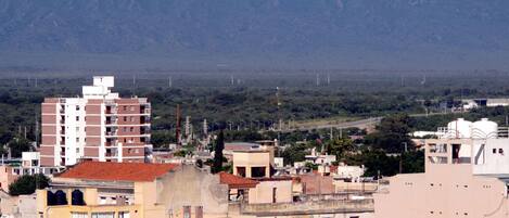 Paisagem urbana com edifícios, incluindo uma estrutura vermelha e branca em destaque, e uma cadeia de montanhas ao fundo.