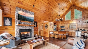 Un intérieur chaleureux de chalet en bois, avec une cheminée en pierre, des meubles en bois, un coin cuisine et de grandes fenêtres.