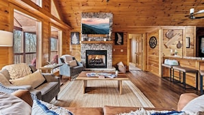 Un intérieur de chalet chaleureux avec une cheminée en pierre, des murs en bois et un coin salon confortable.