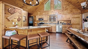 Une cabane en bois rustique dotée d’une cuisine comprenant un grand îlot central, des tabourets de bar et une table à manger.