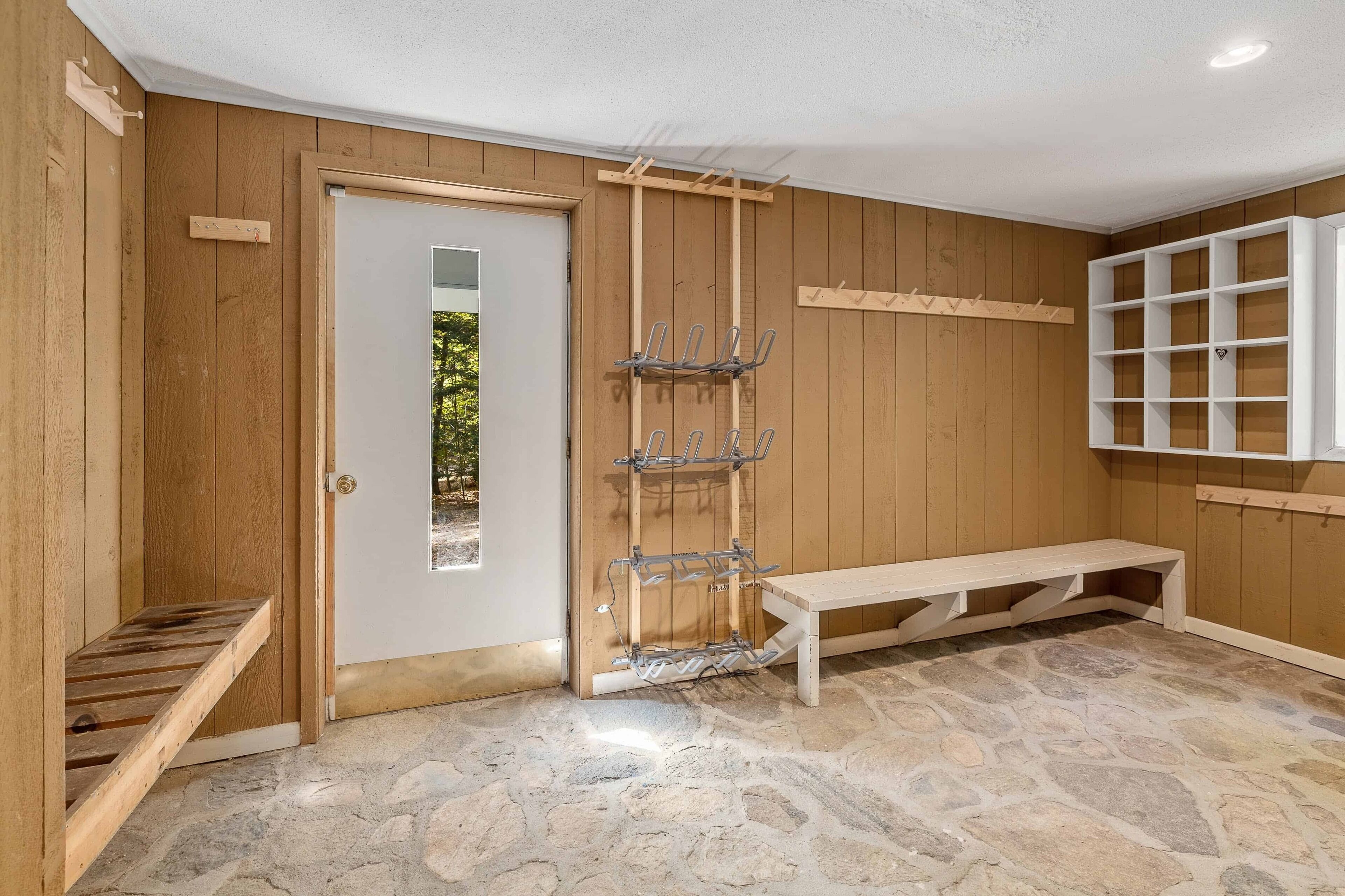A room with wooden walls, a stone floor, a bench, and a wooden door.
